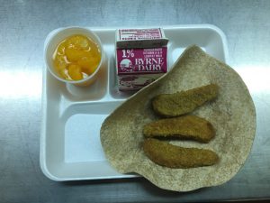 peaches in a fruit cup, low fat white milk, taco shell & chicken tenders on a tray