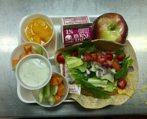 tray with carrot & celery sticks with dressing, apple, peaches, milk, chicken wrap topped with fresh veggies
