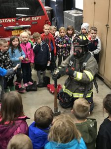 students gather around a fireman dressed in turnout gear
