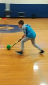 student using roll of wrapping paper to scoot ball across the gym