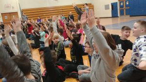 students seated on floor, hands in the air