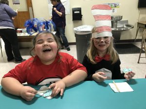 two students in cafeteria wearing Seuss headgear and eating frosted crackers