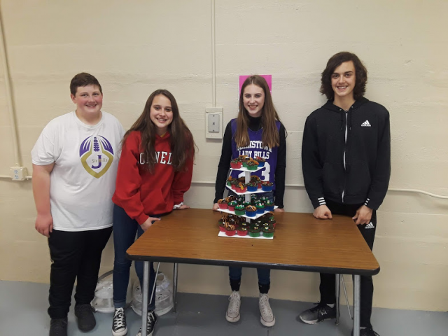 four students standing behind a table with a cupcake display