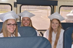 students in caps & gowns on a school bus