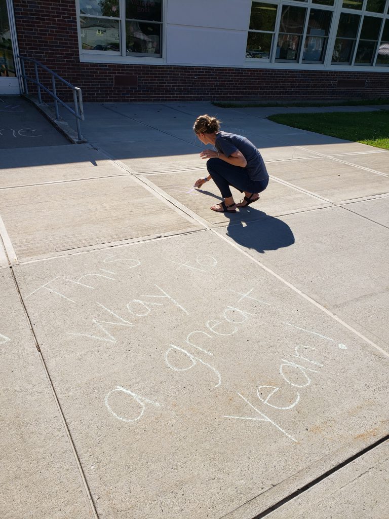 woman kneeling on sidewalk to write with chalk