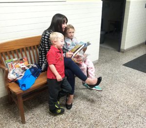 parent seated on bench reading with two children