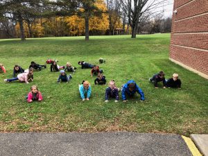 group of students on the lawn outside of school doing push ups