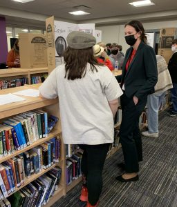 an adult woman chats with a young student about their class project on display in the library