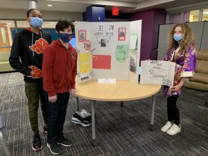 two boys and a girl stand in front of their school project on display in a library