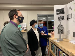an adult male wearing a face mask looks at a student's project on display in the library