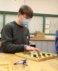 a male student wearing a face mask and protective eye gear plays checkers