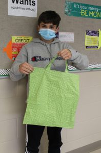 a young boy wearing a face mask shows off a green bag that he made