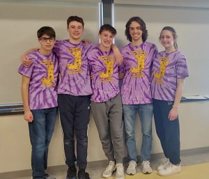 four young men and one young woman pose for the camera wearing purple team t-shirts with a yellow "J" on the front