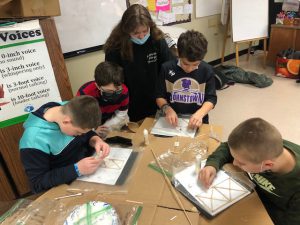 four male elementary students work on a project as they are supervised by one teacher