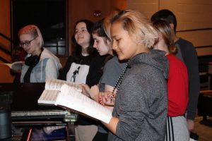 student actors rehearse a song around a piano