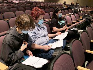 students sitting in theater chairs make notes in a script