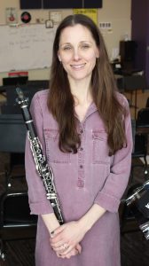 a woman wears a purple dress, holding a clarinet in a music room