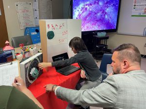a young boy shows a teacher his science presentation
