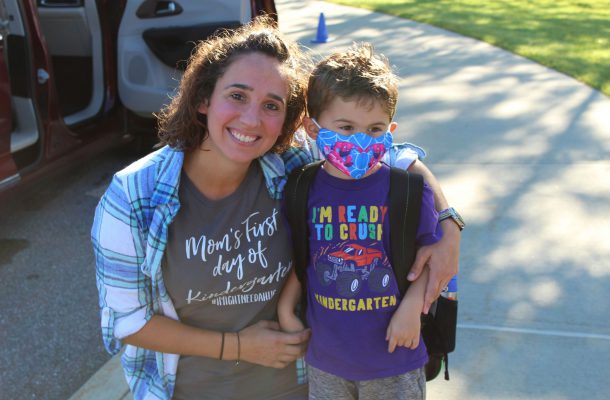 a mom leans down to pose with her son on his first day of school