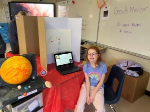 a girl with glasses sits in front of her science project