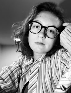 a black and white photo of a young woman wearing a striped top and glasses