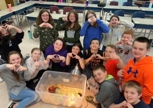 students pose around a plastic container with baby chicks in it