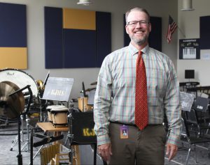 a man wearing a tie and glasses stands in a music room