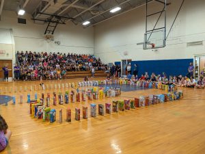 students are in a gymnasium for an assembly to watch a maze of cereal boxes knock each other over