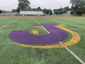 a turf field shows a purple and gold J logo
