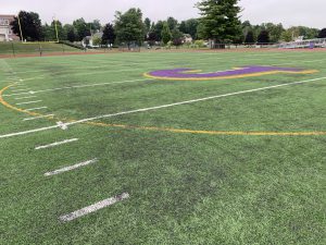 a close-up shot of turf field showing football yard markers and a purple J logo