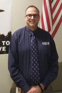 a man wearing glasses and a tie poses next to the American flag
