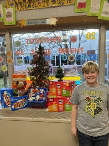 student standing next to boxes of snacks and a small Christmas tree in a window