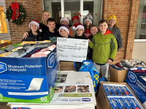 students pose with handwritten check and boxes of gifts purchased for nursing home residents