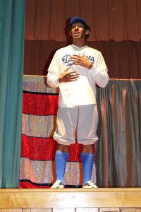an actor wears a baseball jersey and portrays the character of Jackie Robinson on a stage 