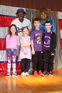 four elementary students pose with two actors on a theatrical stage