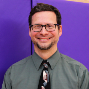a man wearing a green shirt with a tie stands in front of a purple wall