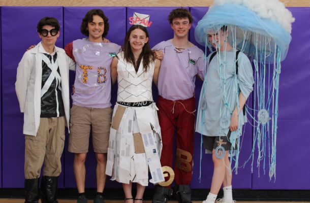 five teenage students pose in front of a purple wall