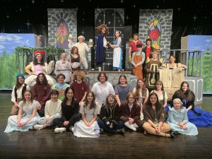 a group of teenaged actors pose together in costume on a theatrical set