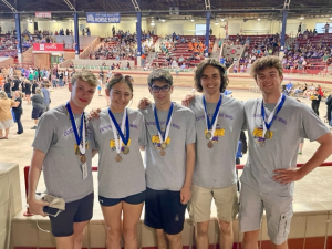 a group of students wearing grey t-shirts and medals around their necks, pose in an arena