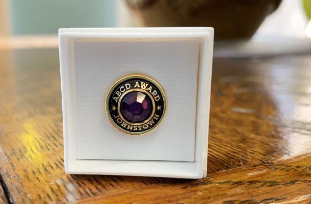 a pin showcasing a purple gemstone is shown in a jewelry box