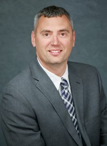 a man with grey hair wearing a grey suit, white shirt and tie