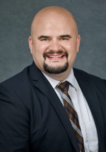 a bald man with facial hair wears a suit and tie