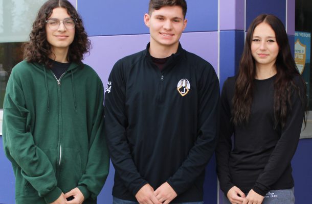 two male students and one female student pose outside their school, in front of a purple wall