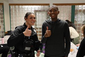 a police officer poses with a student as they both give a "thumbs up" gesture