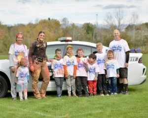 three adults pose with several children in front of a police car, after completing a color run.
