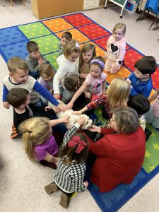 young students sit on a carpet and pet a dog