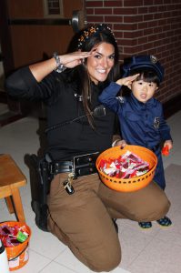 a police officer poses with a child dressed as a police officer for Halloween, as they both salute