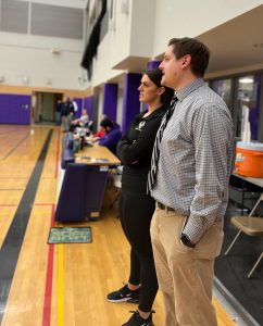 a woman stands next to a man in a gymnasium as they coach a team from the sidelines