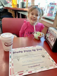 a young girl sits at a table and eats ice cream