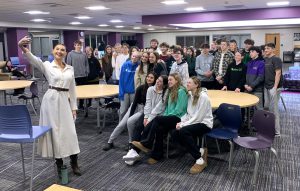 a woman in a white dress takes a selfie with a group of students behind her